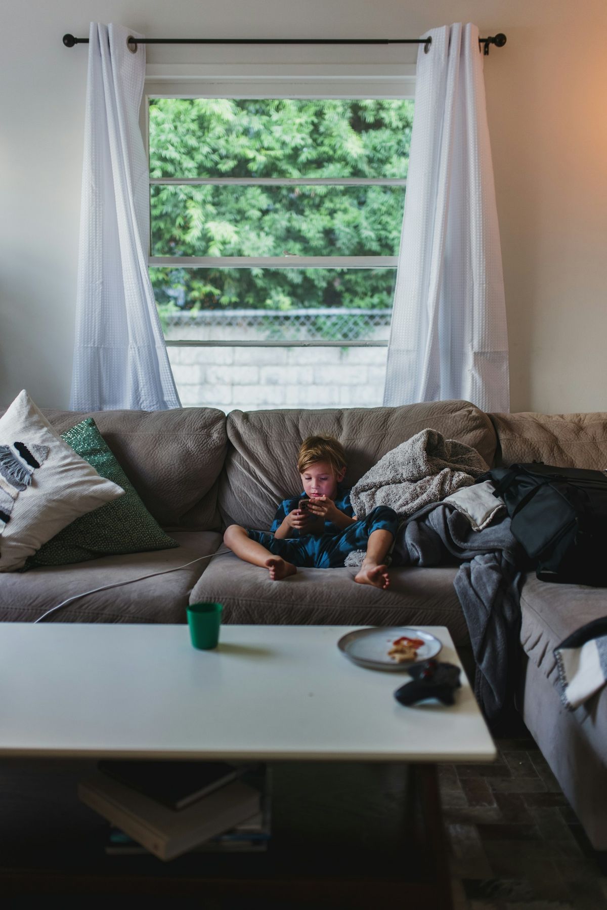 Gutt i pysjamas hviler i sofaen med teppe og drikkeglass