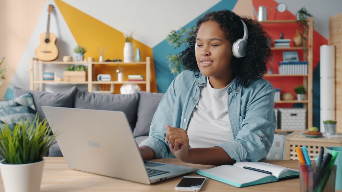 Ung kvinne med hodetelefoner ved laptop og notatbok hjemme
