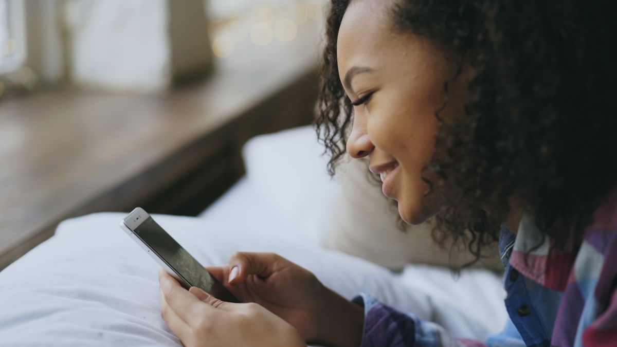 Ung kvinne leser på mobiltelefonen i sengen