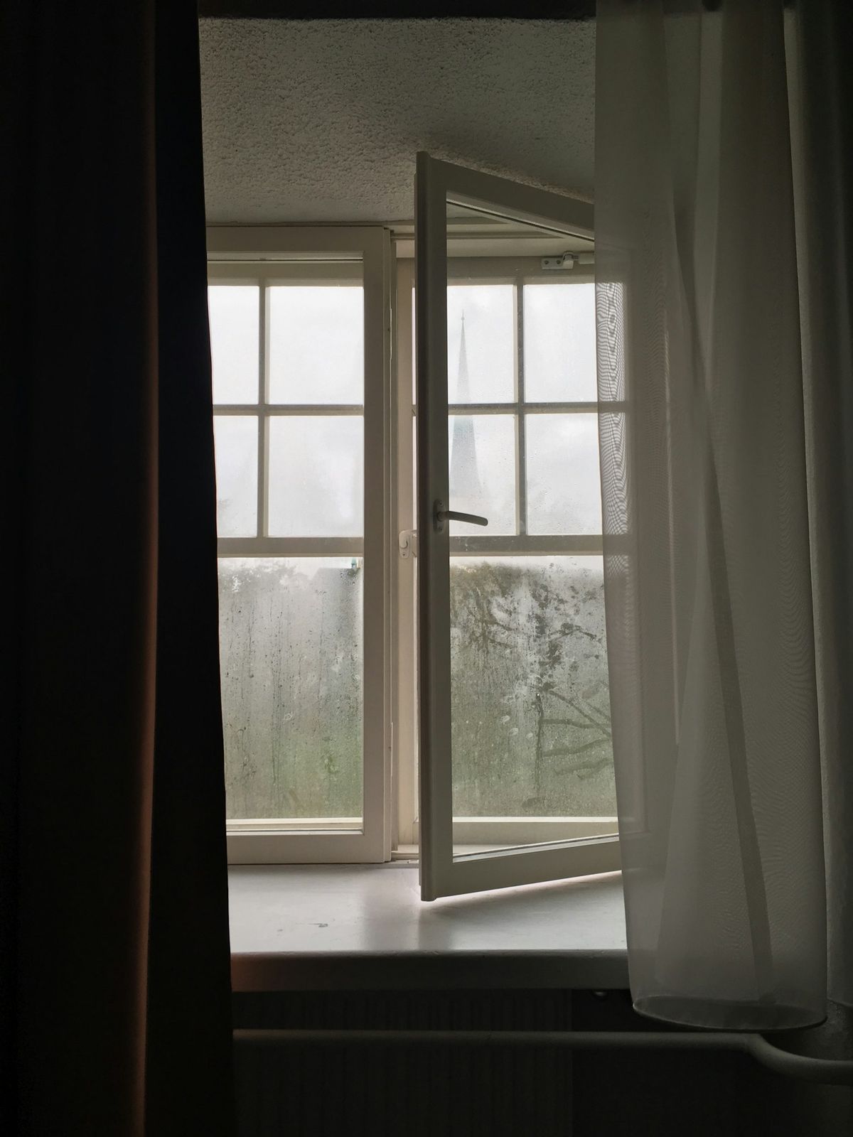 Apent vindu innenfra med lett gardin ved karmen