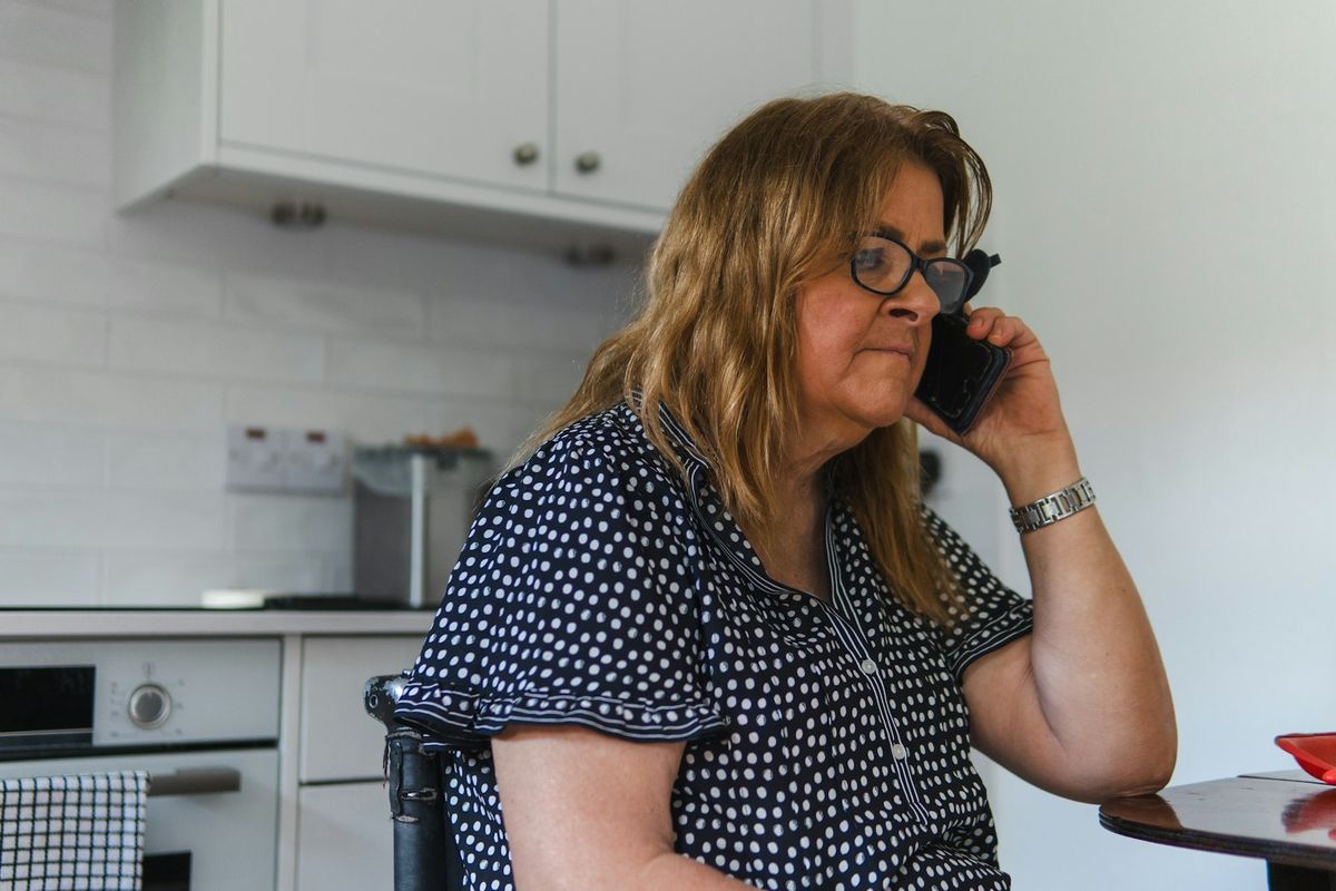 Kvinne med briller sitter på kjøkkenet og snakker alvorlig i mobiltelefon